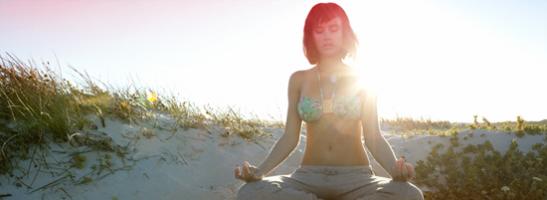 Billede af en kvinde der sidder på stranden og mediterer. Billedet illustrerer, at det er muligt at slappe af og leve normalt selv når du har menstruation.