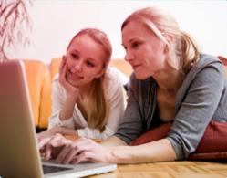 Billede af mor og datter siddende foran en computer. Billedet illustrerer hvordan en mor hjælper sin datter med at finde oplysninger om den første menstruation på nettet.