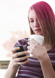 Billede af en pige, der drikker en sodavand, mens hun taler i mobiltelefon.